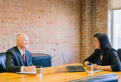 A man and a woman talk across a board table.